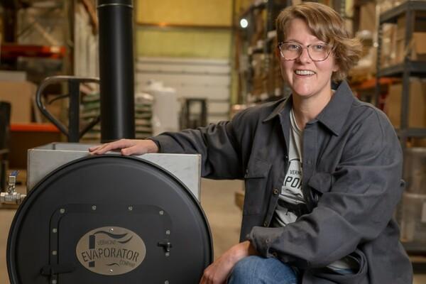 Person smiling in a workshop, hand on a large metal drum.