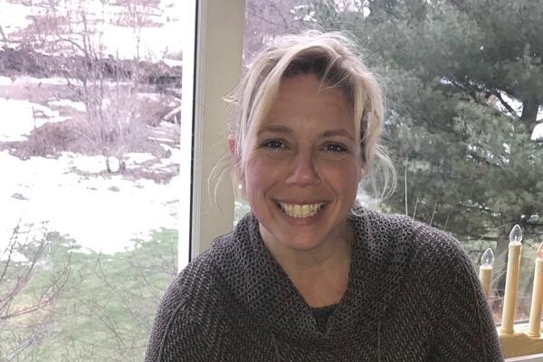 Smiling woman indoors with snowy landscape outside the window.