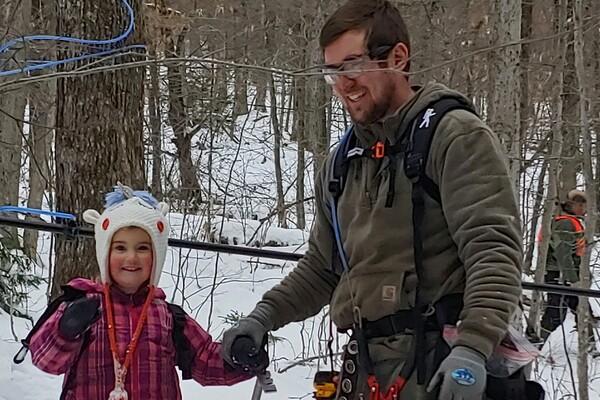 Child and adult in winter clothes smiling in snowy forest.