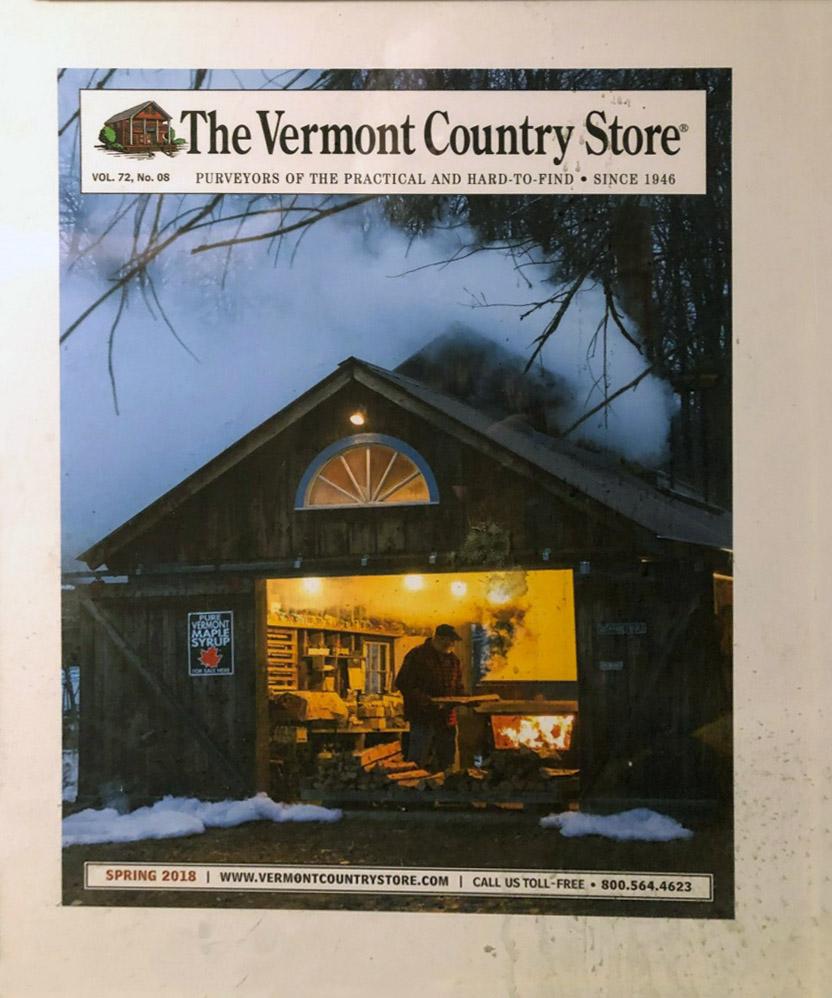 Cozy wooden store at dusk, warmly lit inside, with snow on the ground and trees around.