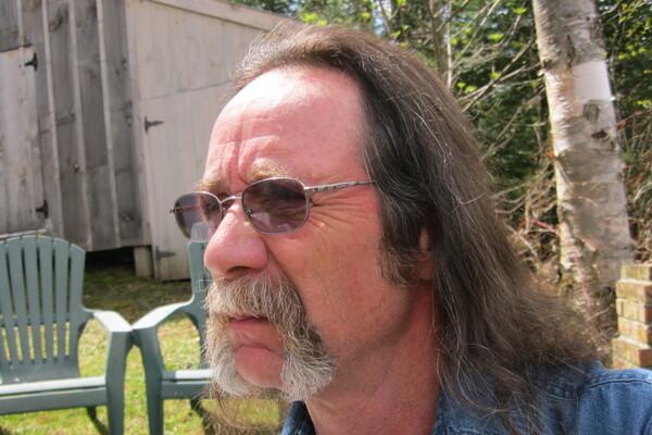 Man with sunglasses and mustache in a garden setting.
