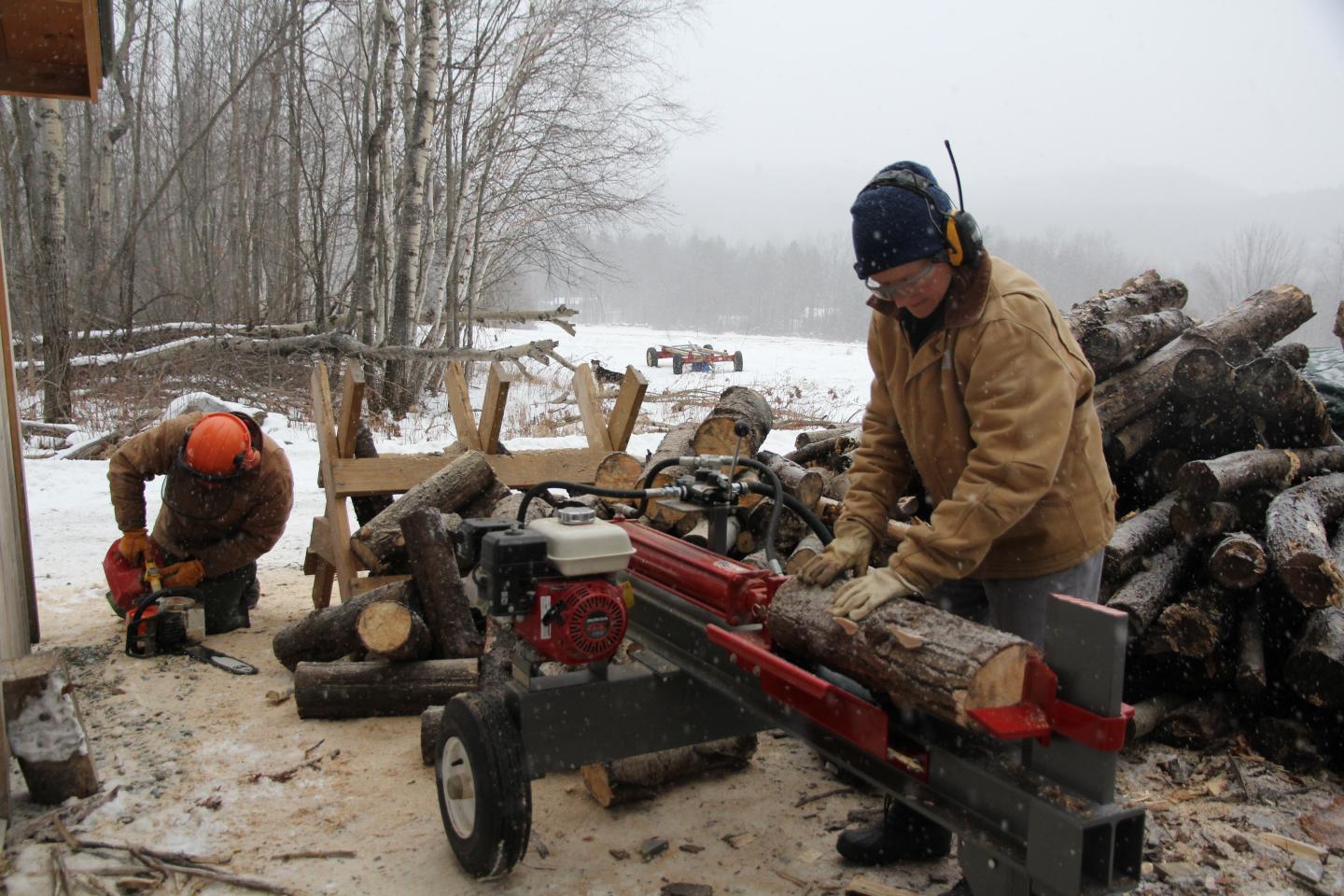 Two people splitting logs with a wood splitter in a snowy setting.