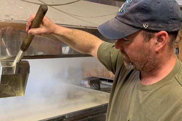Man ladling liquid into a steaming vat.