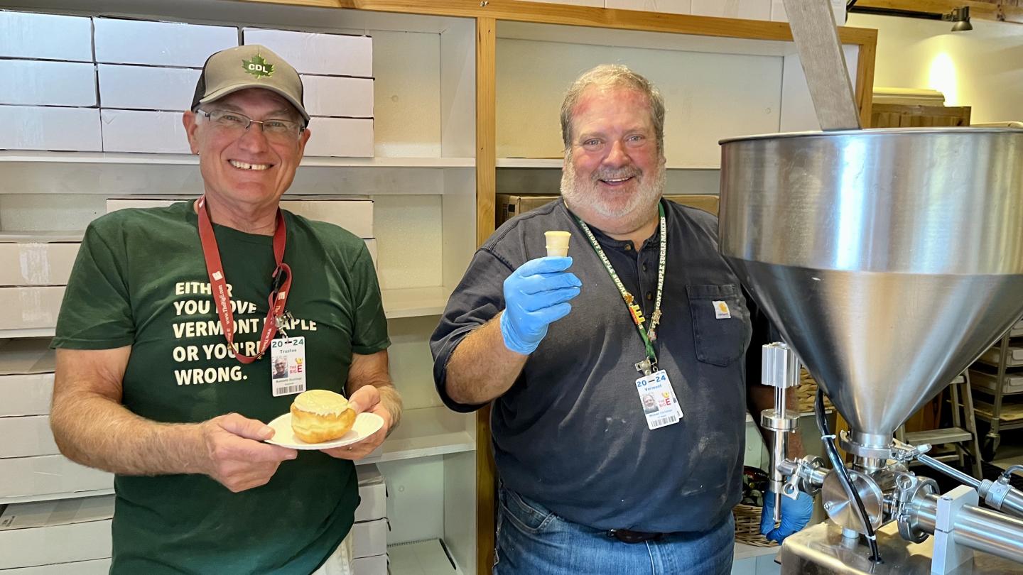 Two smiling men holding ice cream stand next to an ice cream machine.