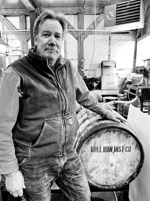 Man standing in workshop beside a large wooden barrel.