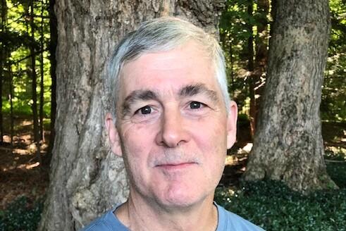 Man smiling in a forest with sunlight filtering through trees.