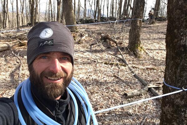 Man in a forest with tubing over shoulder, wearing a beanie and smiling.