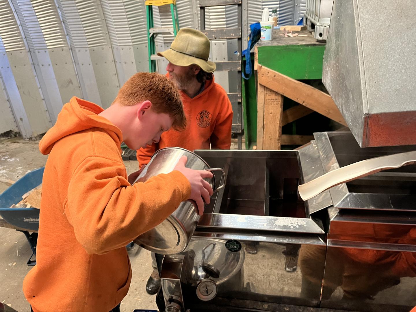 Two people in orange hoodies working with metal equipment in a workshop.