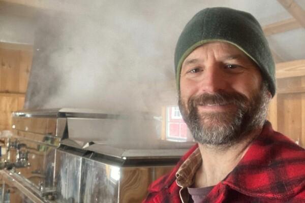 Man in red flannel and beanie in a steamy room with metal equipment.