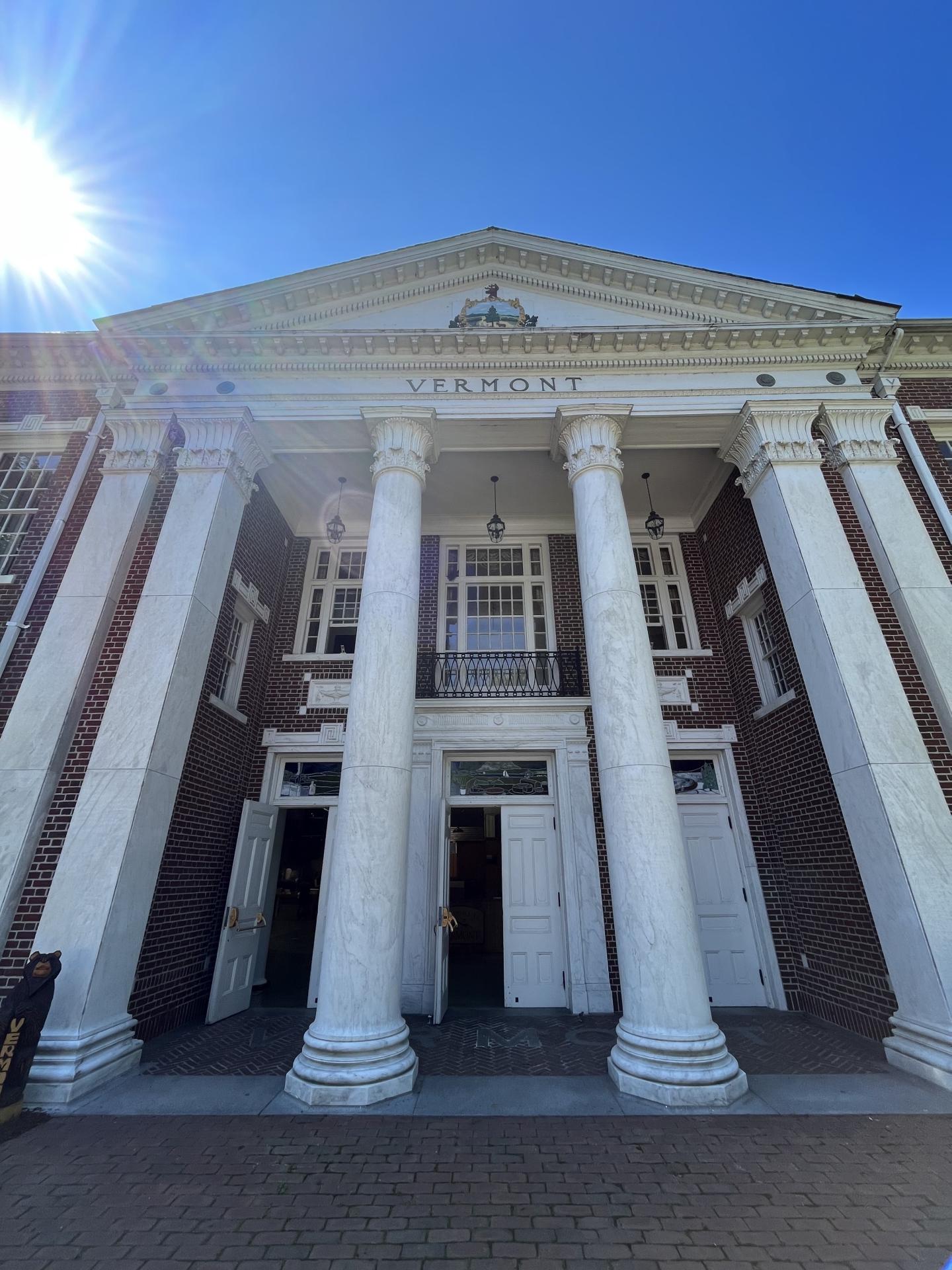 Grand building entrance with tall white columns and sunlight on blue sky.