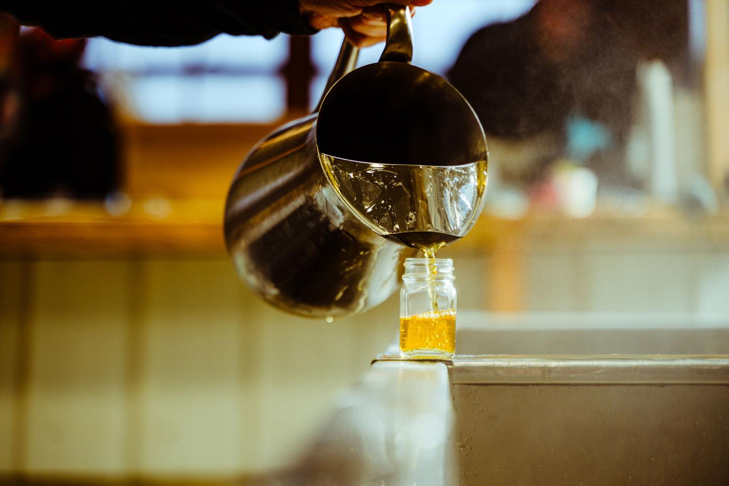 Pouring liquid into a glass jar from a metal pitcher in a warm indoor setting.