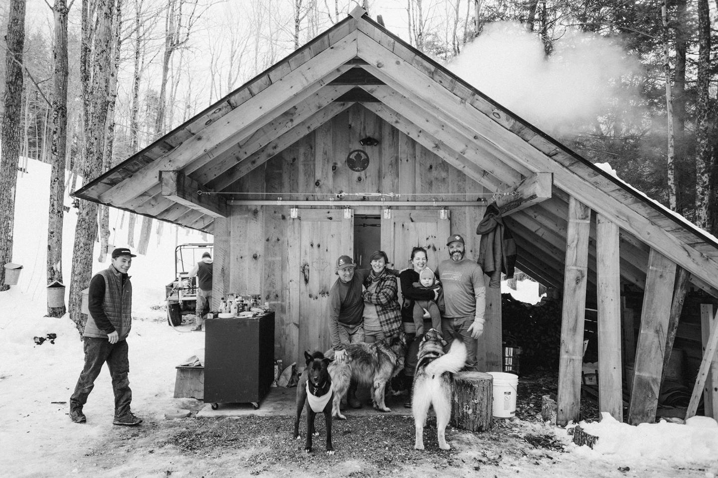 Rustic cabin group photo with three dogs in snowy forest setting.