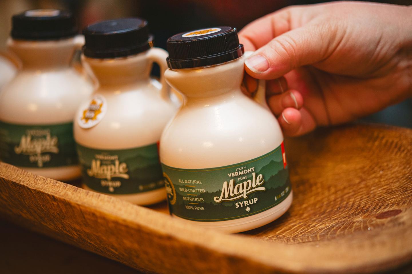 Hand holding a maple syrup bottle on a tray with similar bottles.