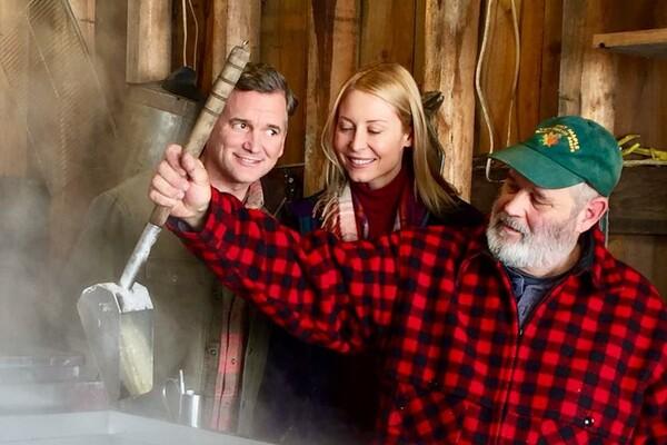 Three people in a rustic setting, watching maple sap boil.
