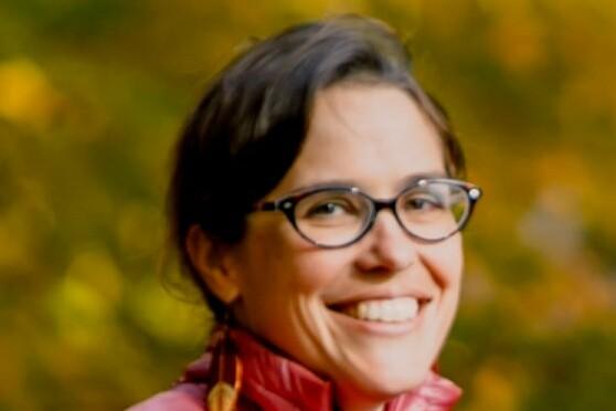 Smiling person with glasses in a red jacket, blurred autumn background.