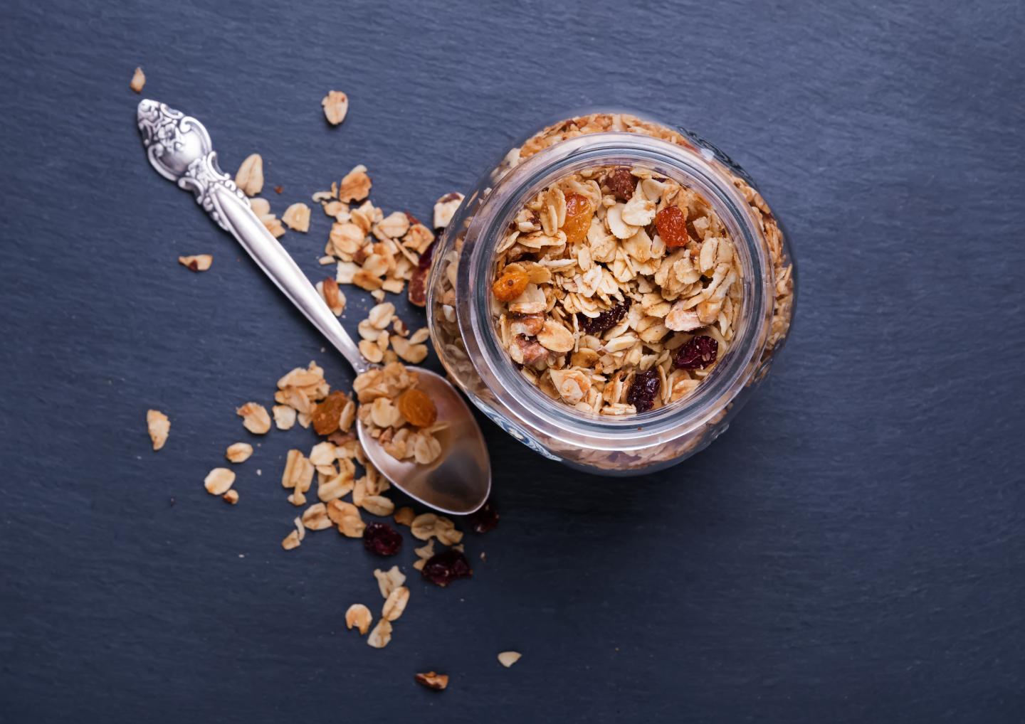 Granola in a jar with a silver spoon on a dark slate surface.