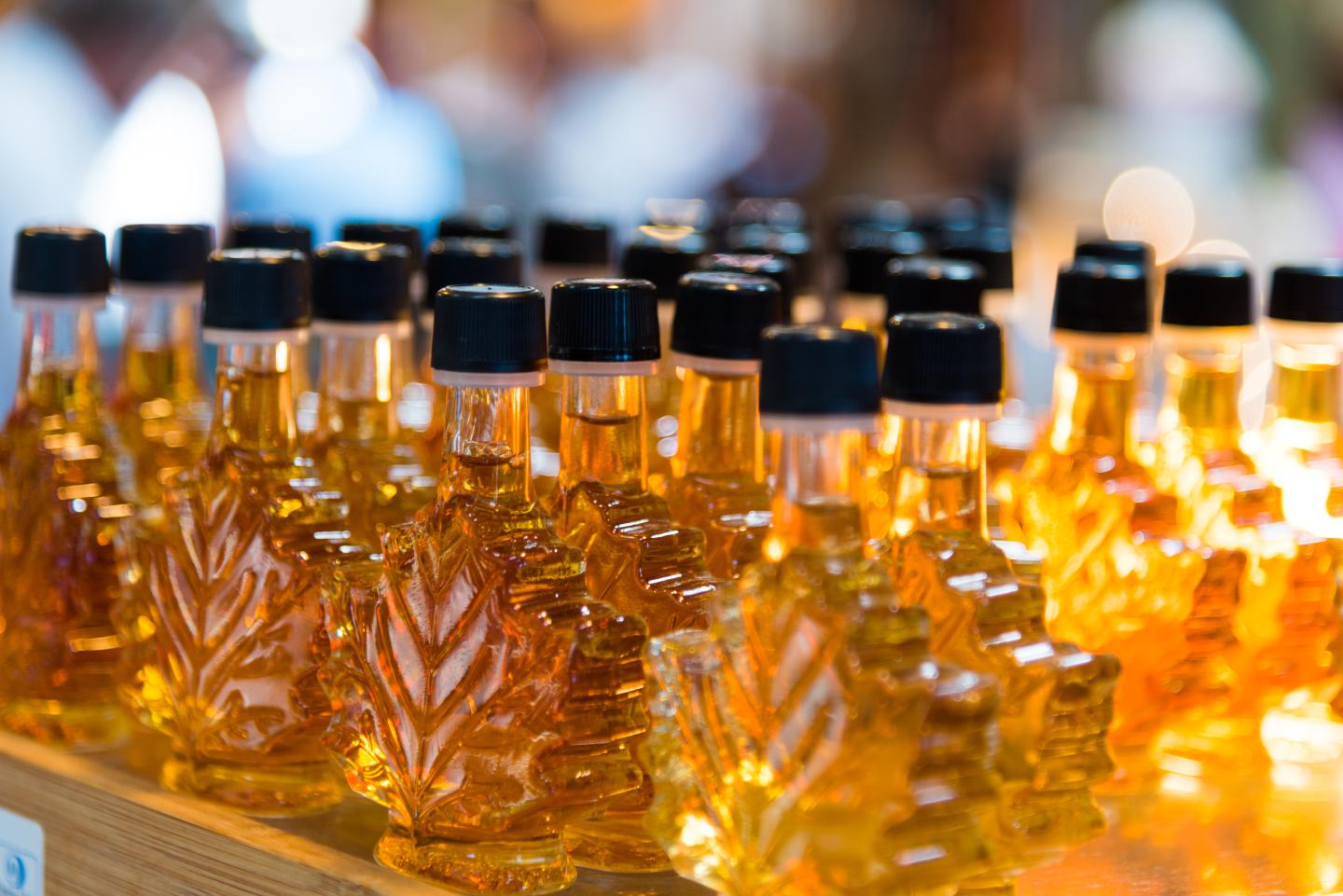 Maple leaf-shaped bottles filled with golden syrup on a wooden shelf.