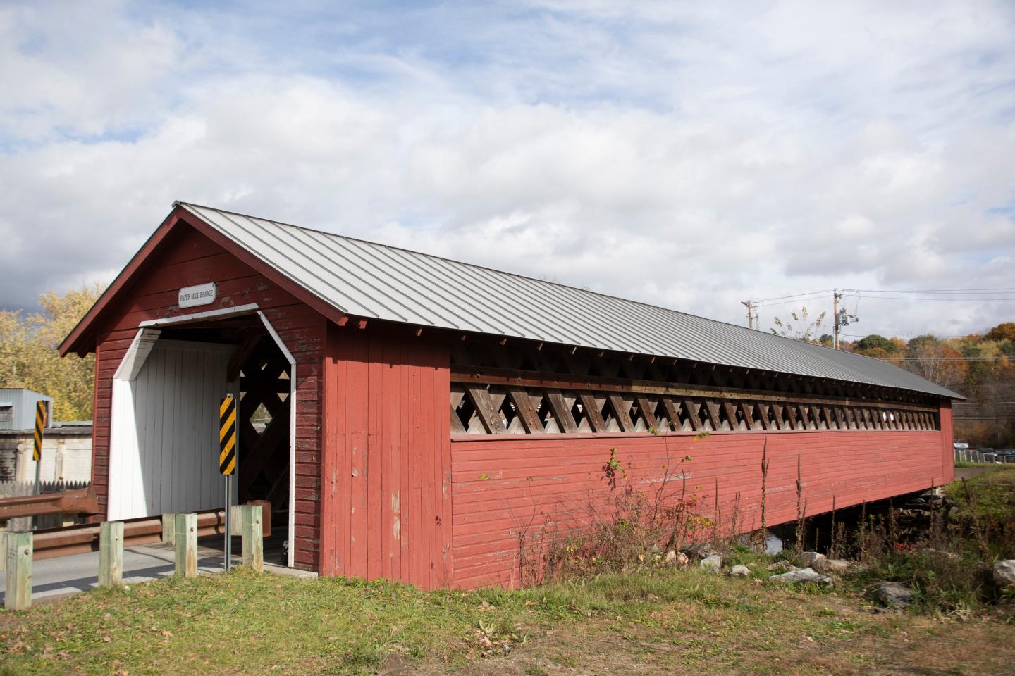 Red covered bridge with a metal roof under a cloudy sky.