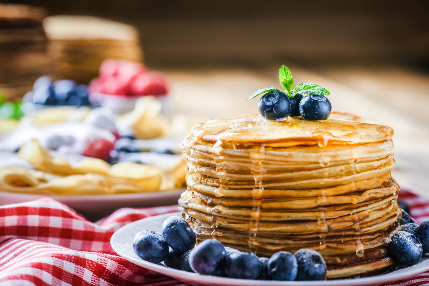 Stack of pancakes with syrup and blueberries on a plate.