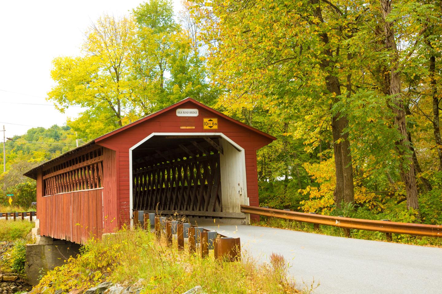 Red covered bridge with autumn trees surrounding it.