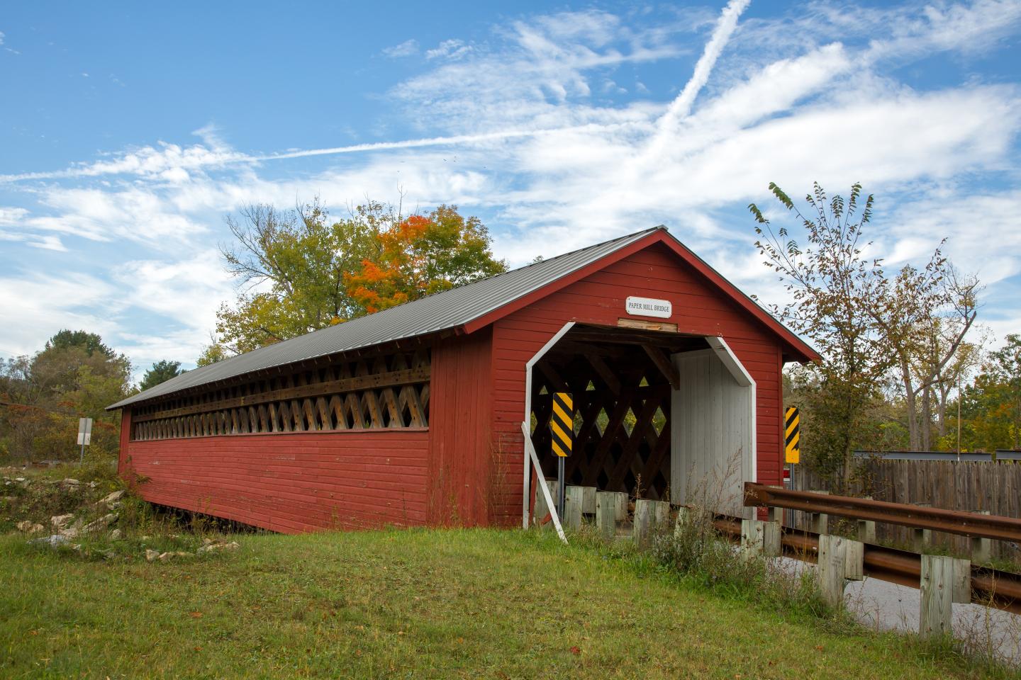 Red covered bridge in a rural setting under a blue sky with clouds.