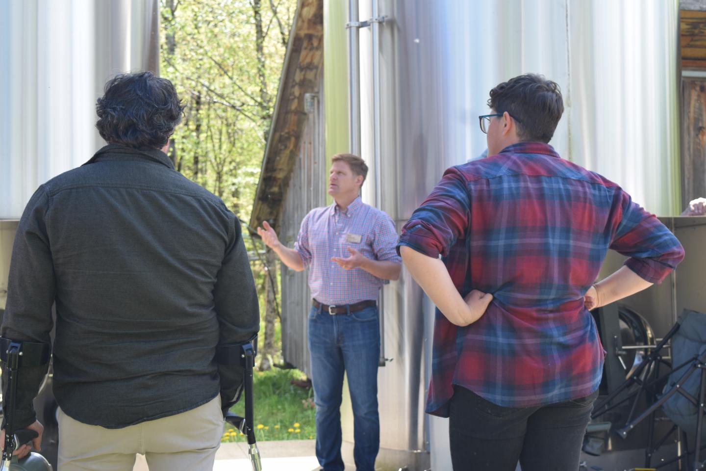Man gives a tour to two people at an outdoor brewery.
