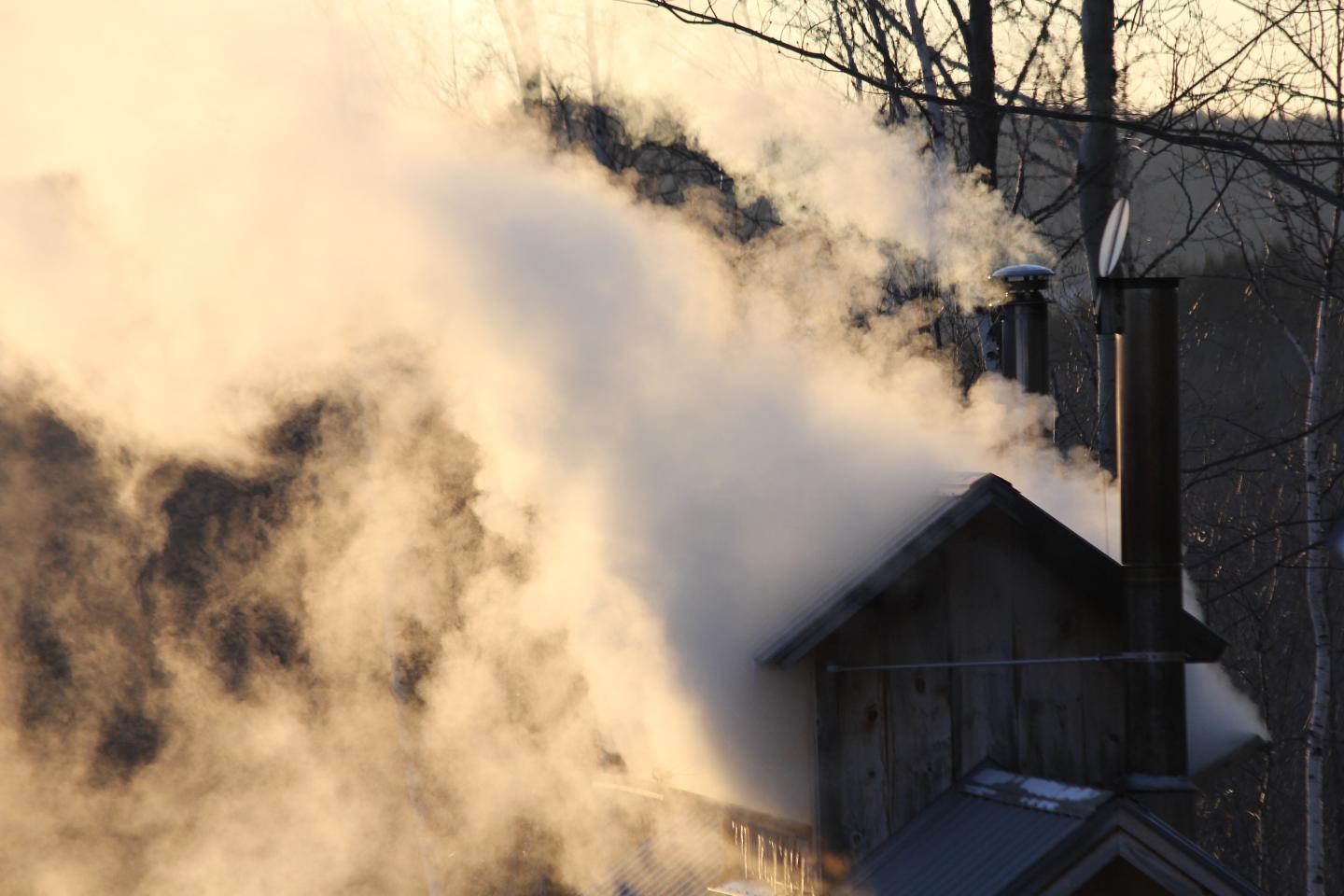 Smoke billows from a chimney on a rustic wooden house at sunset.