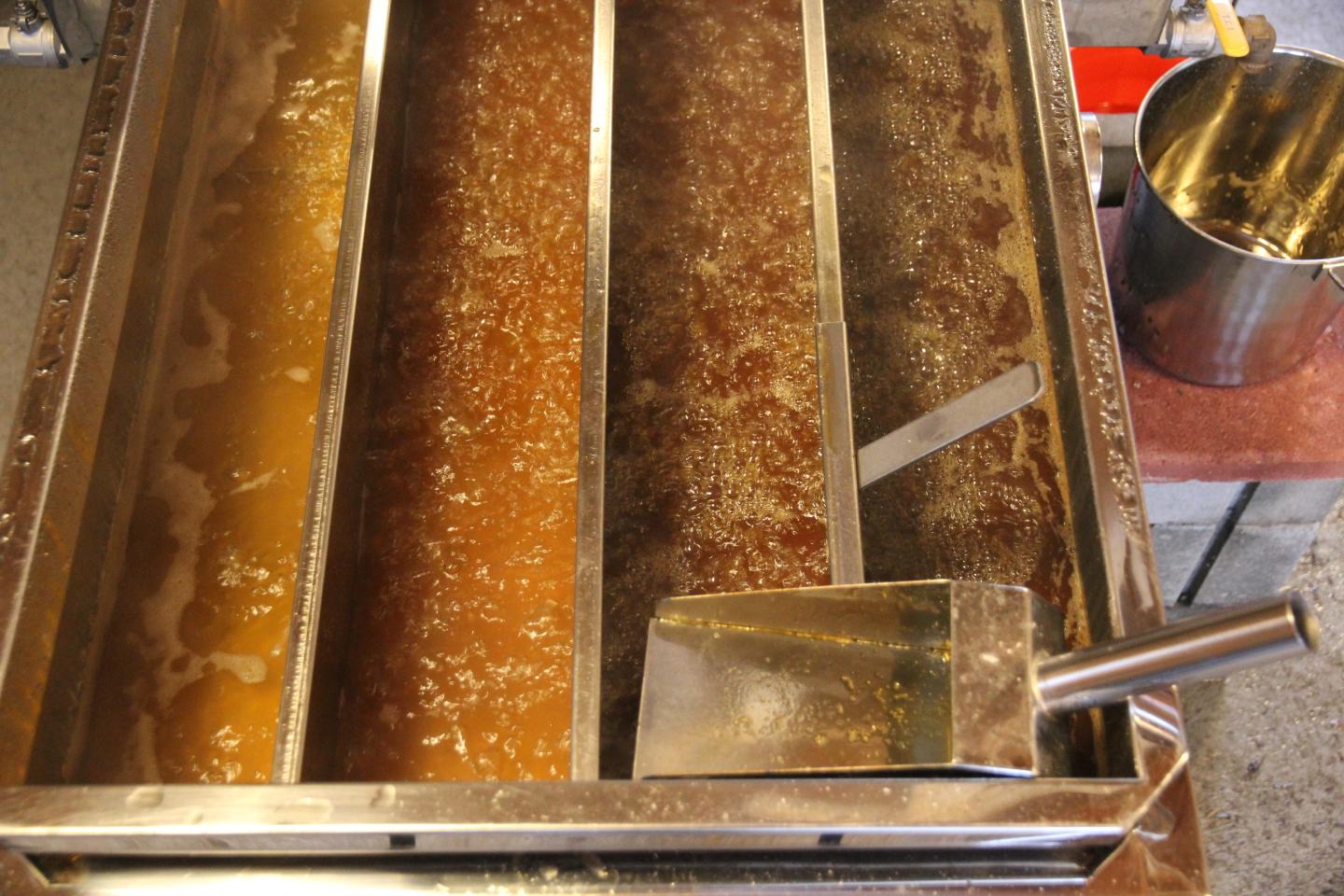 Maple syrup boiling in a stainless steel pan with dividers and a metal scoop nearby.