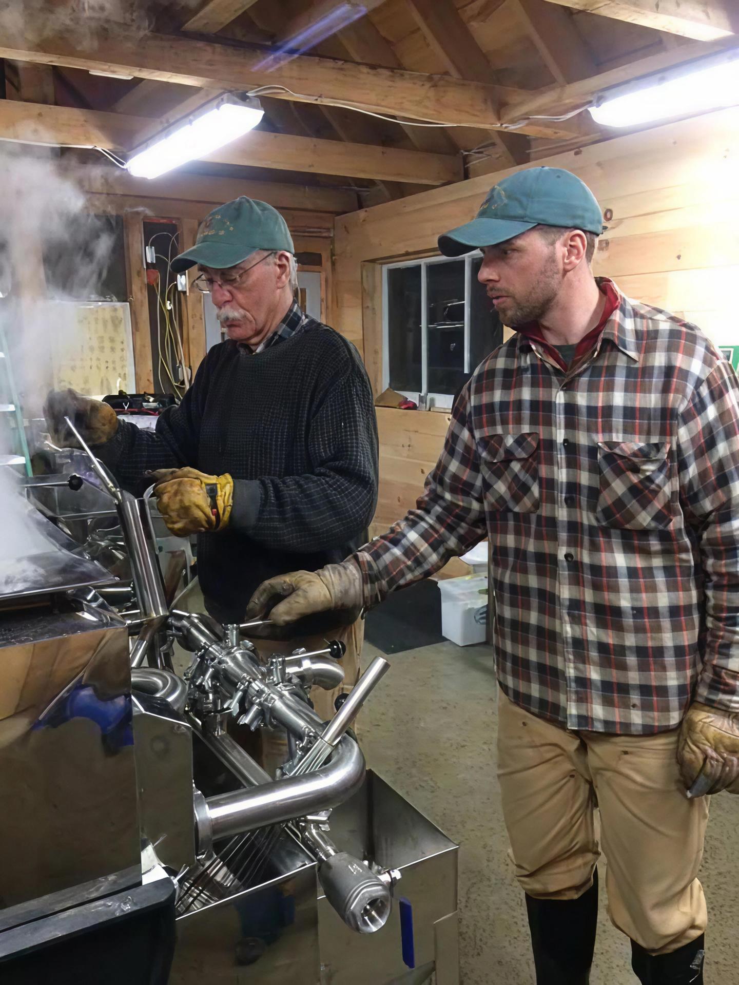 Two men working in a wooden cabin with steaming metal equipment.
