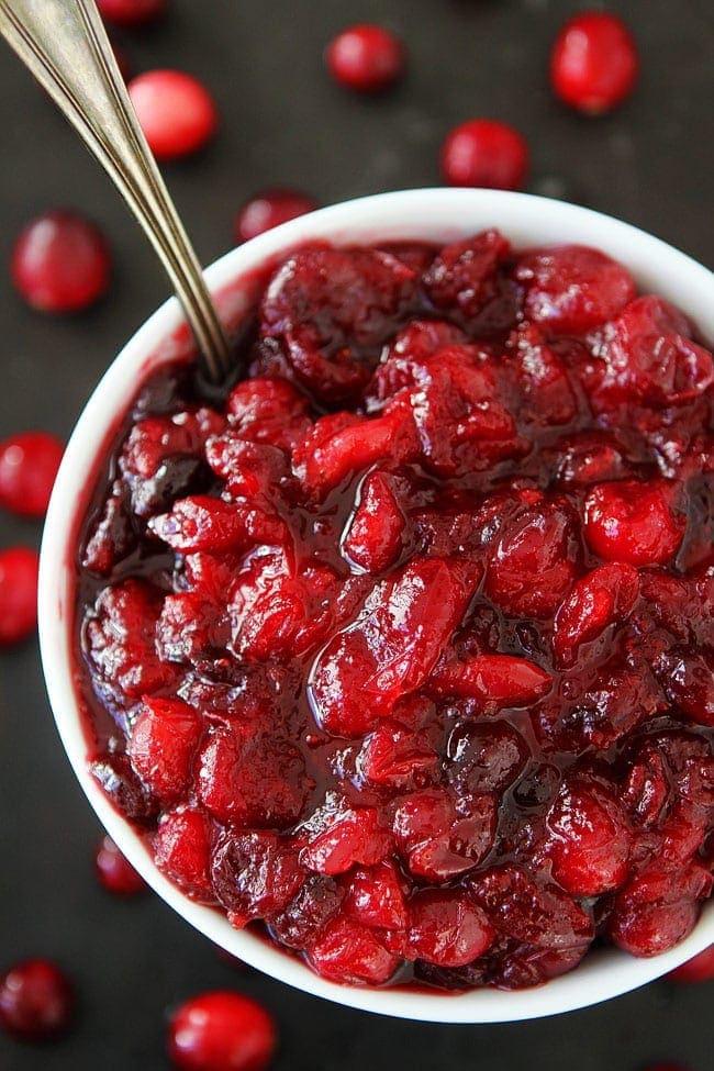Cranberry sauce in a white bowl, surrounded by fresh cranberries.