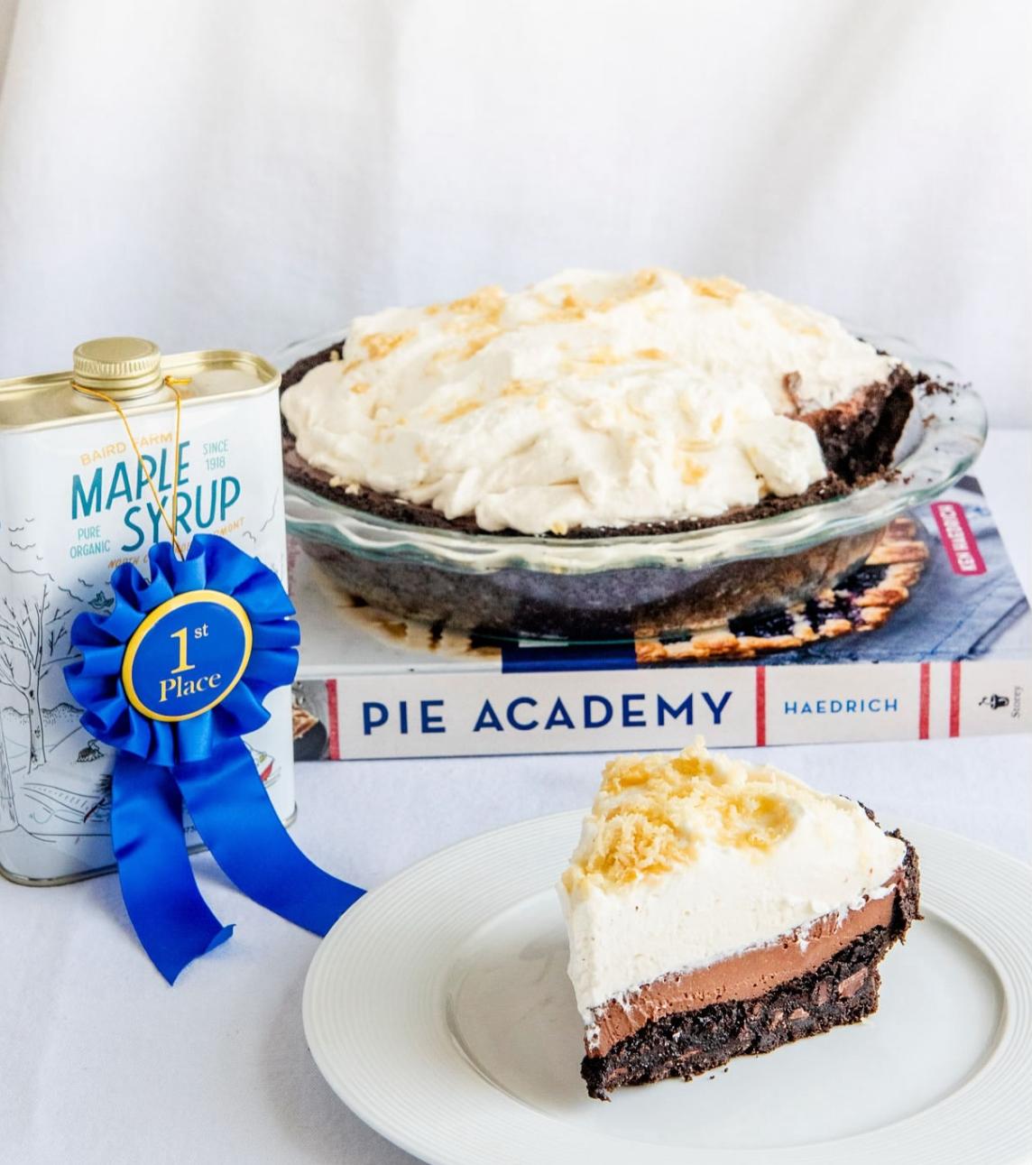 Cream pie with a slice on a plate, next to a syrup can and a blue ribbon.