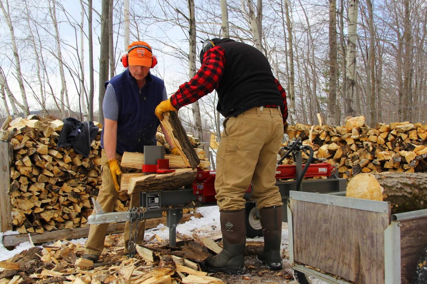 Two people splitting logs with a wood splitter outdoors.