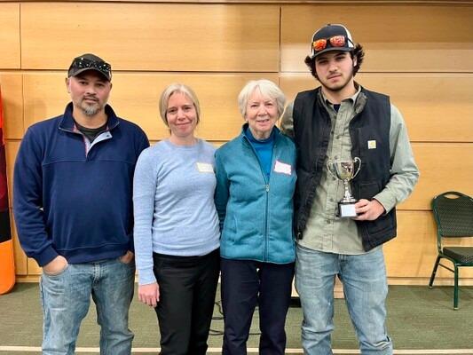 Four people standing together in a hall, one holding a trophy, all smiling.