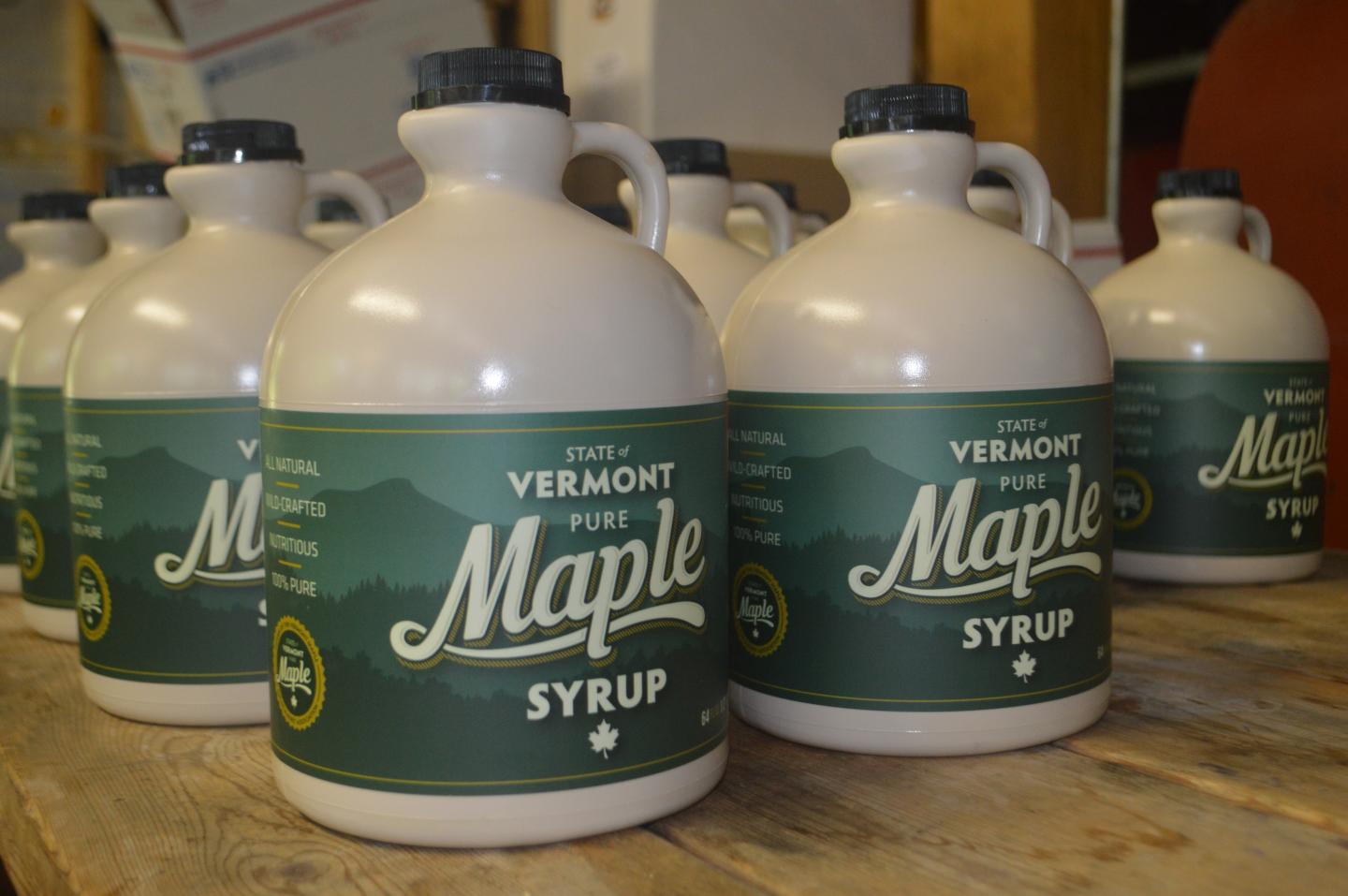 Rows of maple syrup jugs on a wooden shelf.
