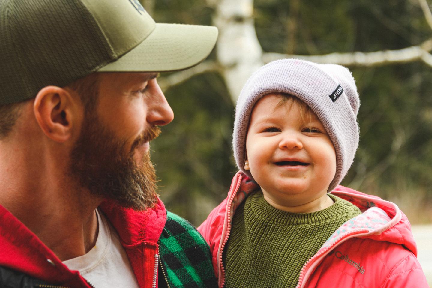 Man and smiling child wearing winter hats outdoors.