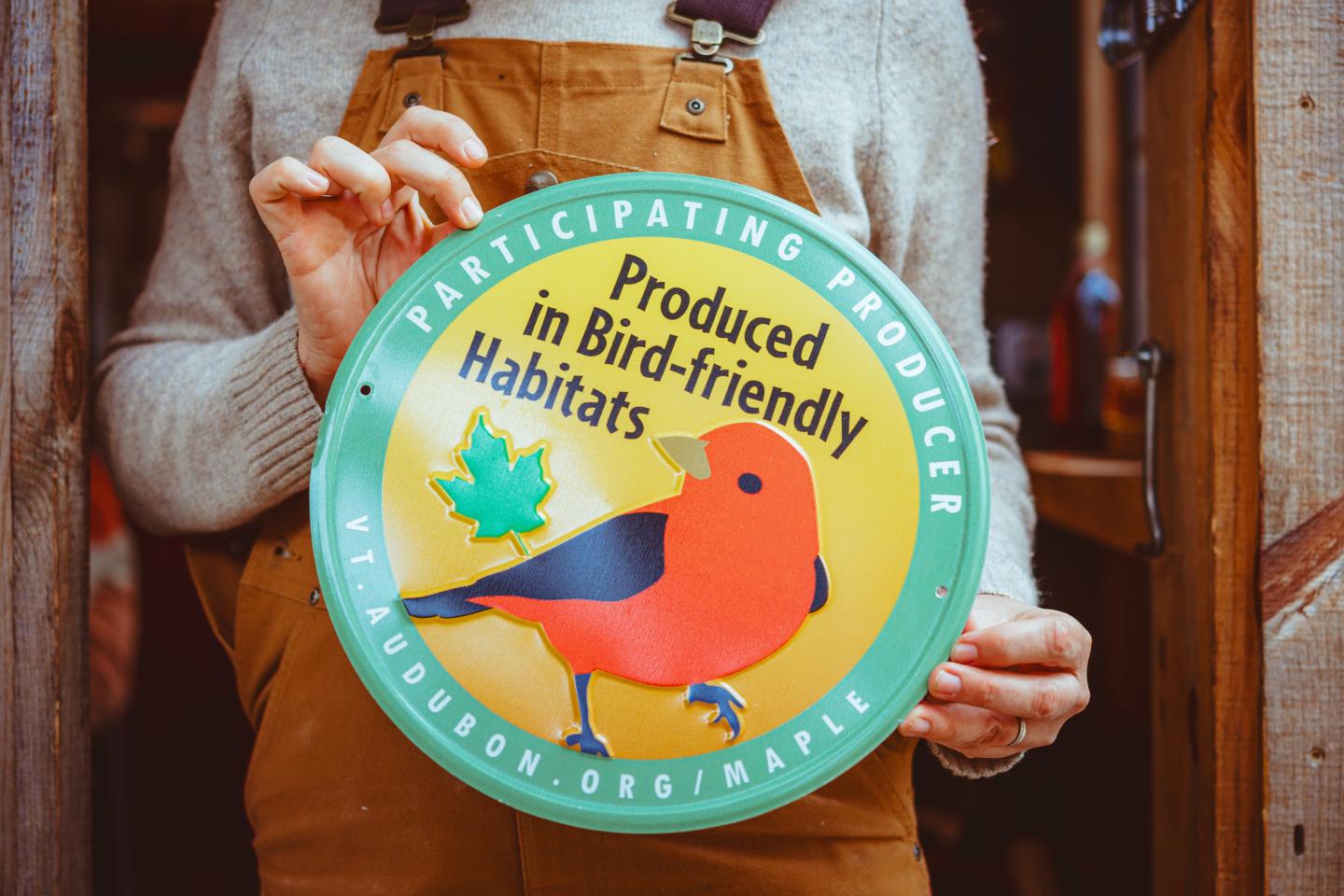 Colorful logo held by person, features a bird and text about bird-friendly habitats.