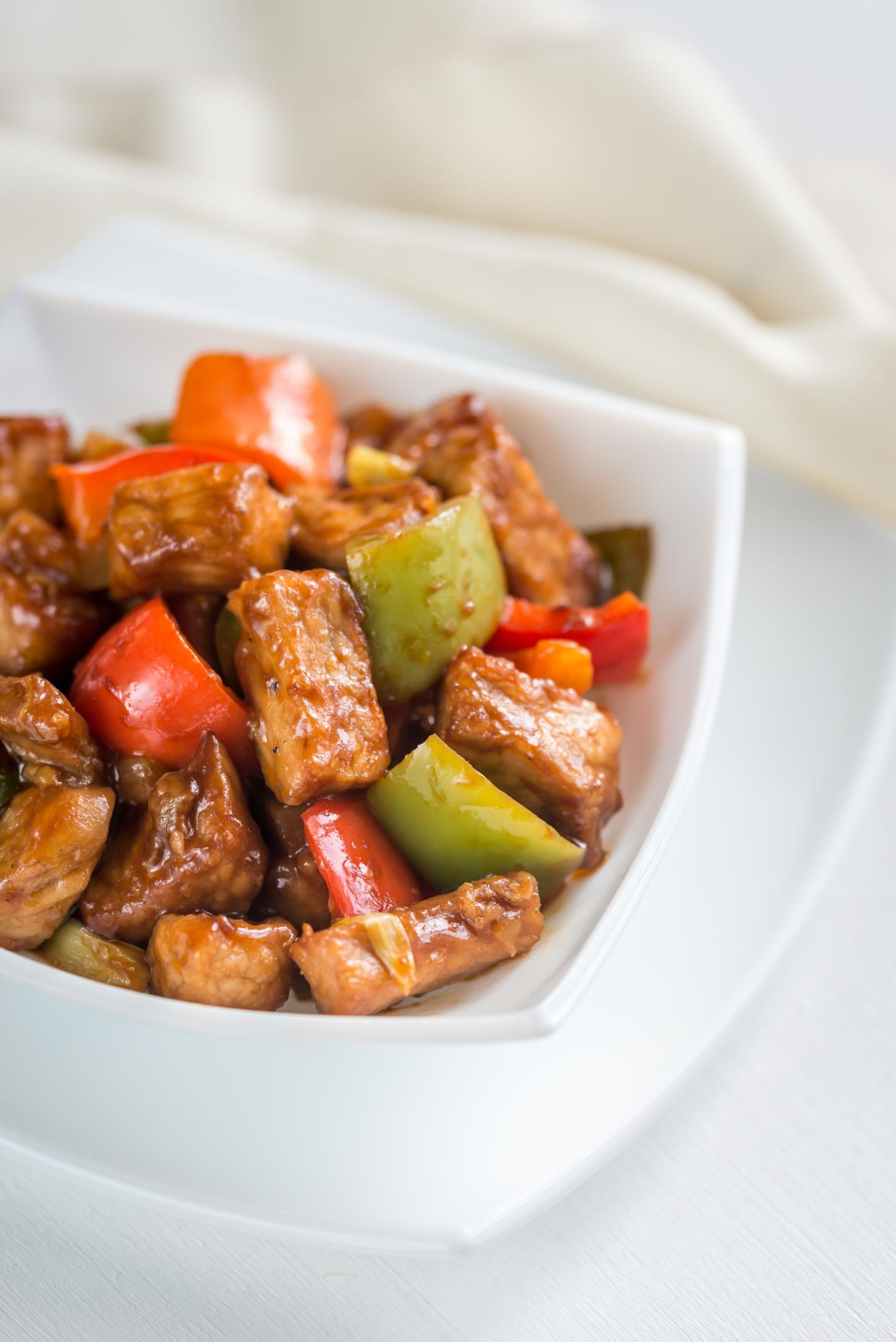 Stir-fried pork with red and green peppers in a white bowl.