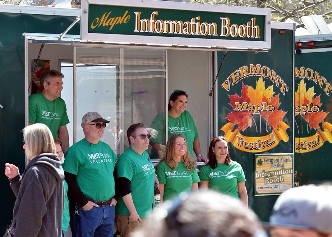 Festival staff in green shirts at a Vermont Maple Festival information booth.