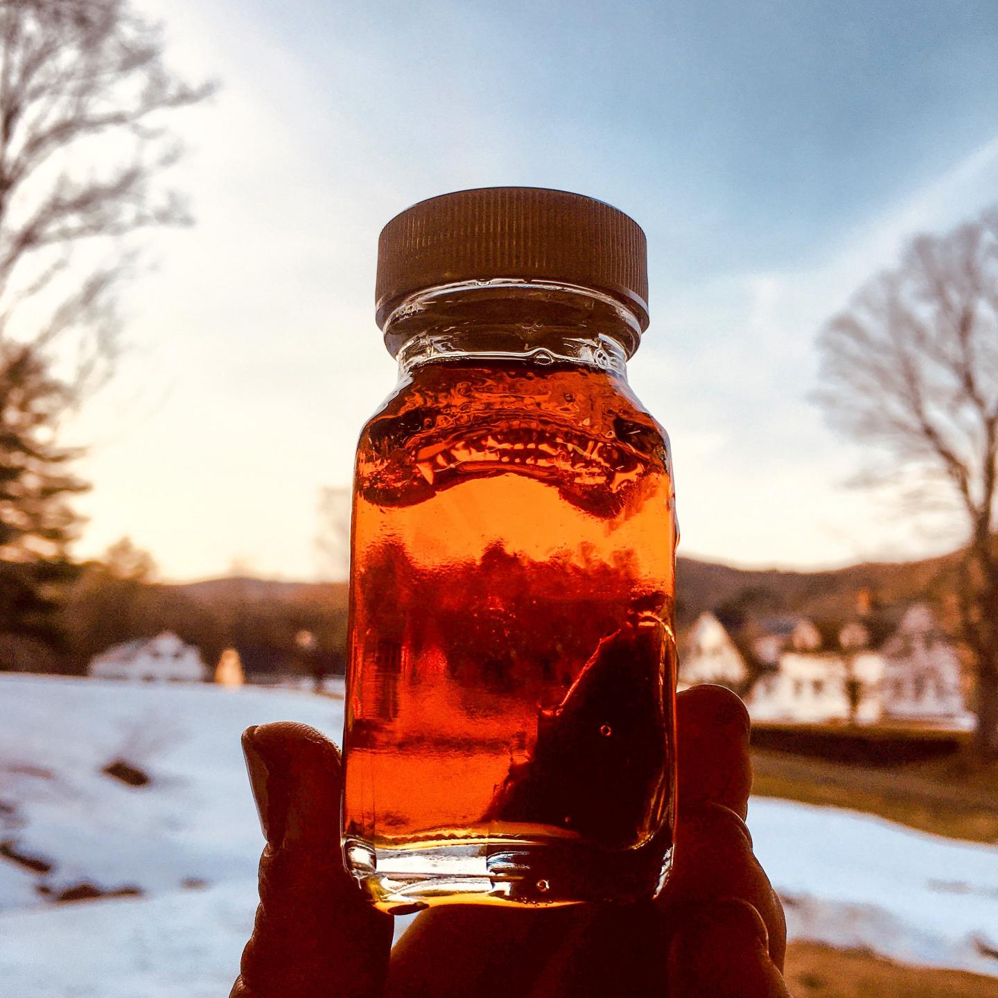Glass jar of amber liquid held against a sunset; snowy landscape in the background.