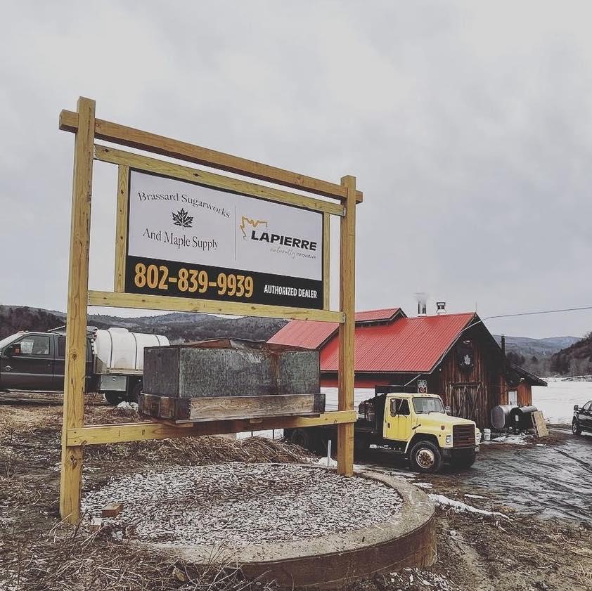 Roadside sign with a phone number, yellow truck, red-roofed building in a snowy landscape.