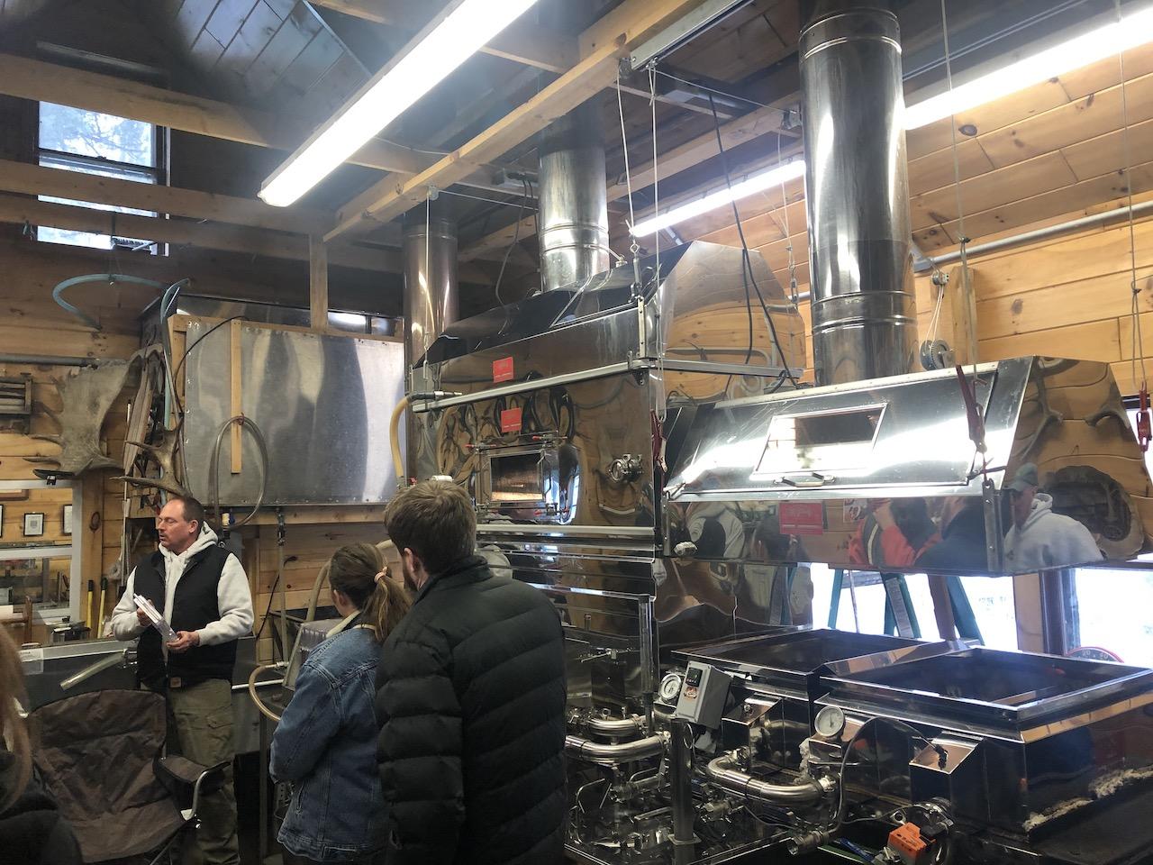 People in a workshop with large stainless-steel syrup evaporators.