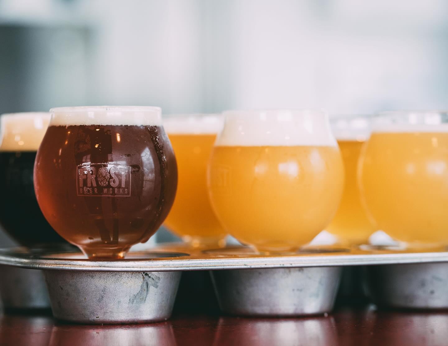 A row of beer glasses, varying from dark to light, on a tray.