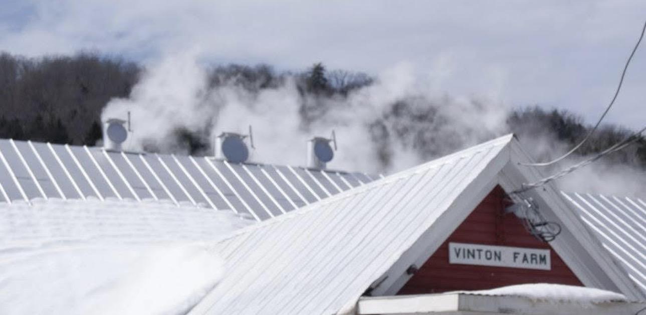 Snowy rooftops with steam rising against a cloudy sky.