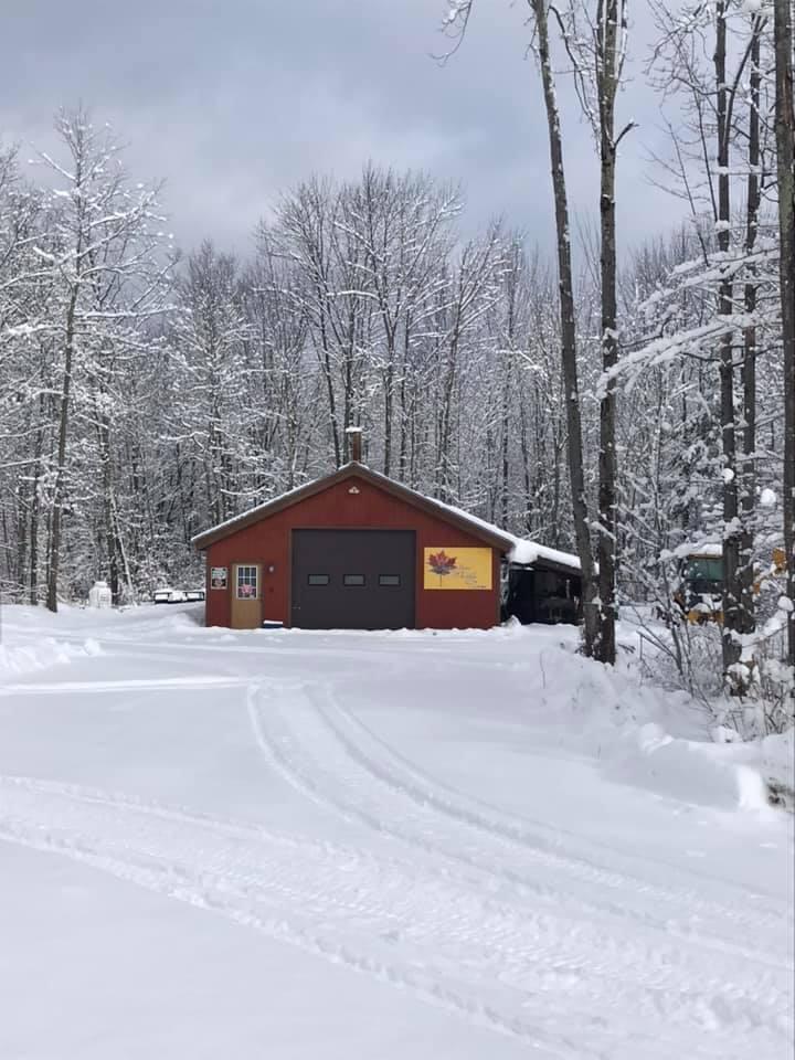 Red cabin in a snowy forest with tire tracks on the ground.