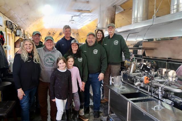 Family posing in a cozy kitchen with industrial equipment and warm lighting.