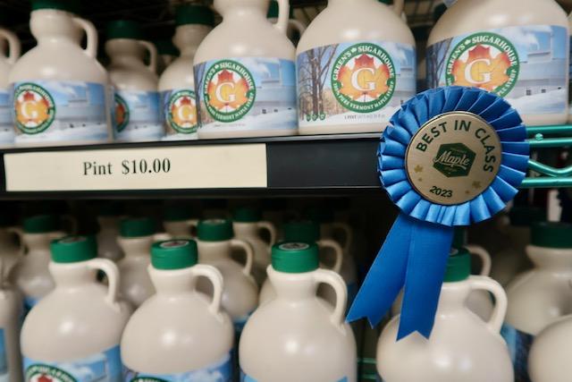 Maple syrup bottles on shelves, blue ribbon labeled "Best in Class."