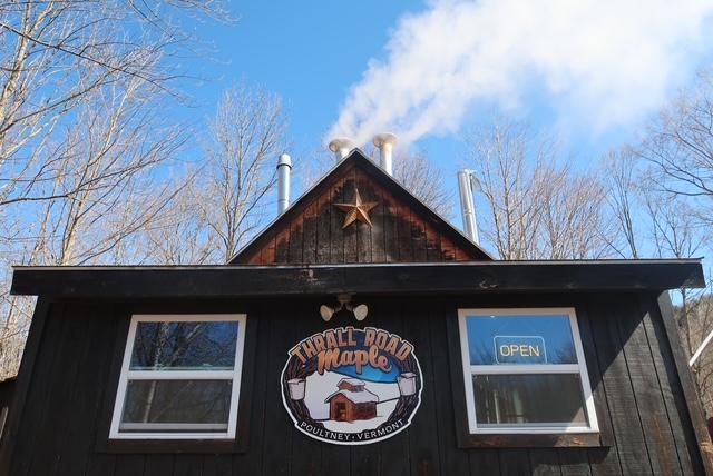 Rustic building with a maple sign, chimney smoke, and a clear blue sky.