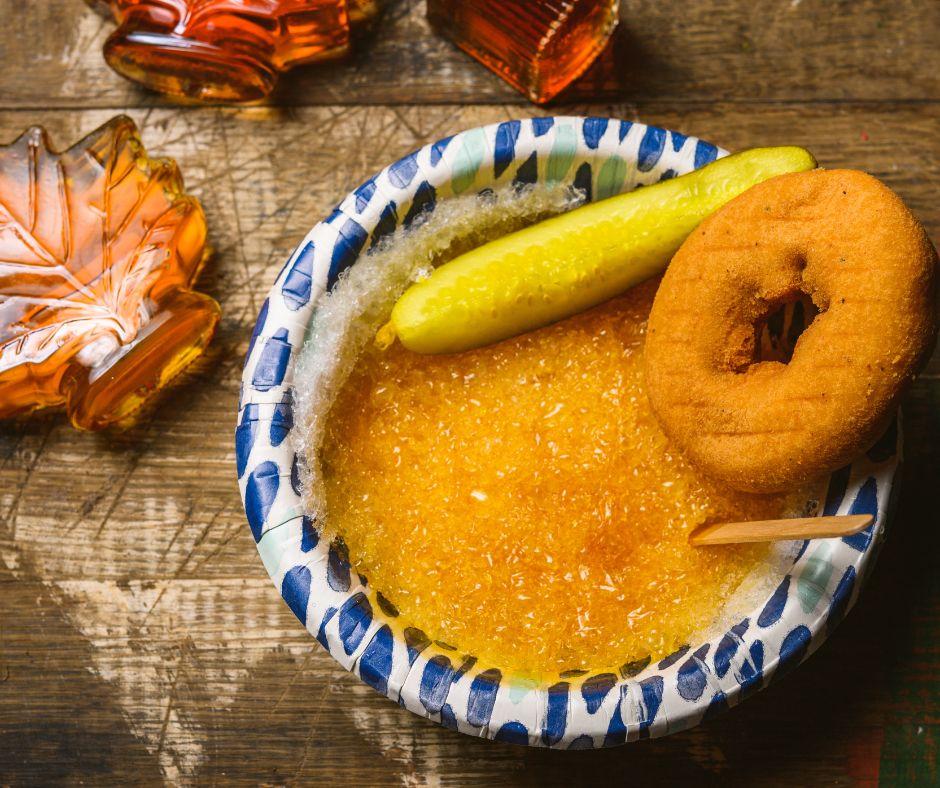 Bowl of sugar on snow with a doughnut and pickle on a wooden table.