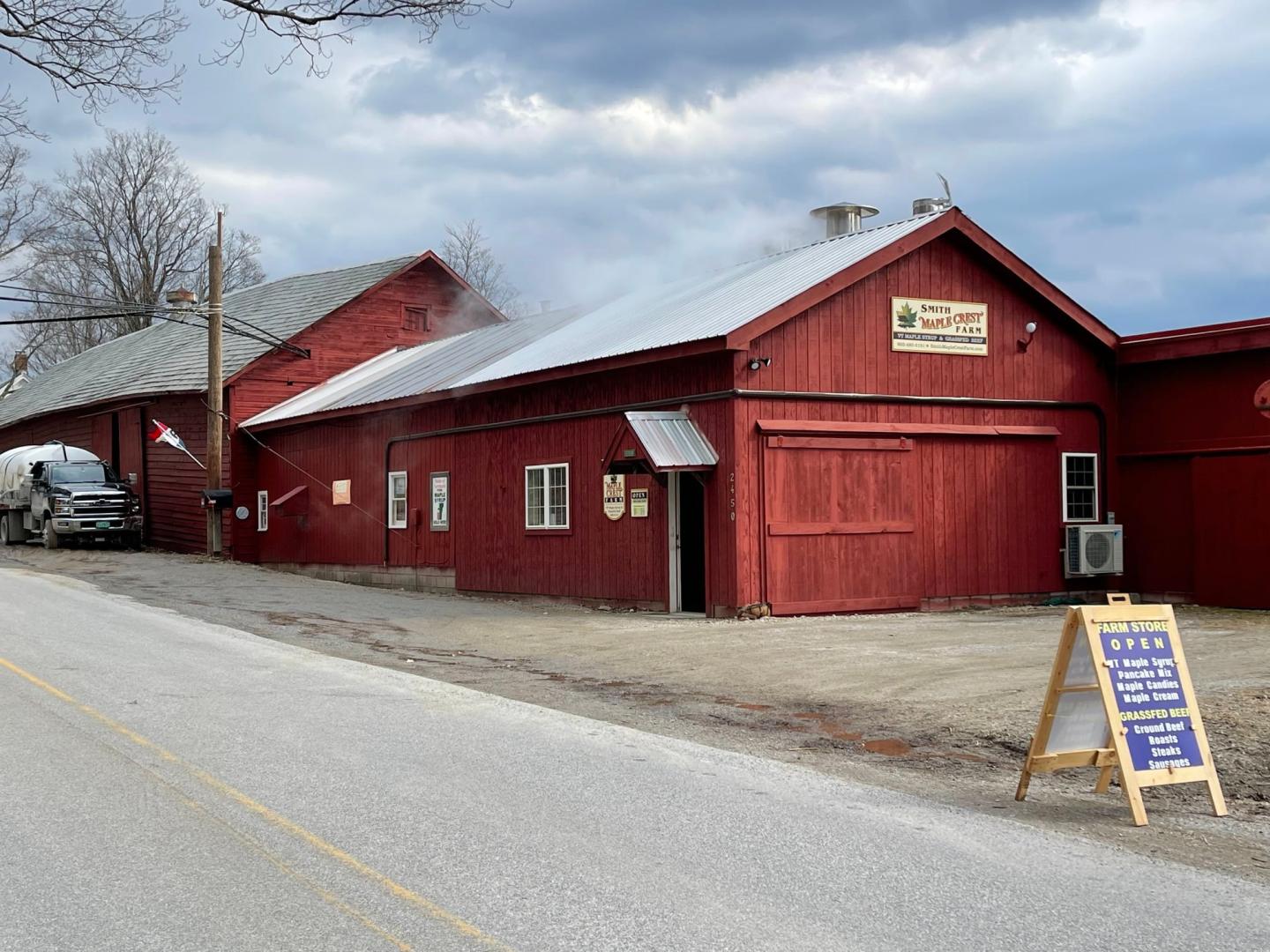 Red wooden building on a cloudy day with a signboard outside.