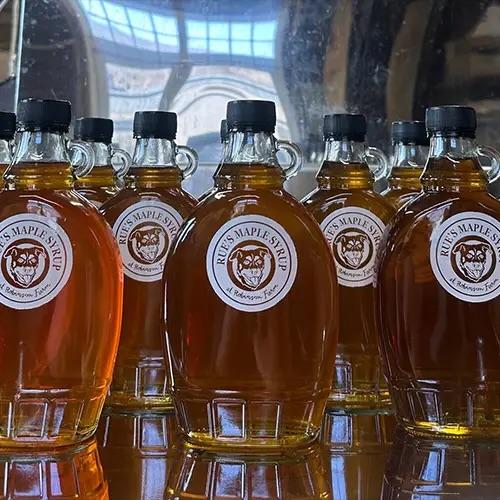 Bottles of amber syrup with black caps, reflected in a mirrored surface.